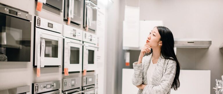Half length portrait of asian woman choosing new oven in furnitu