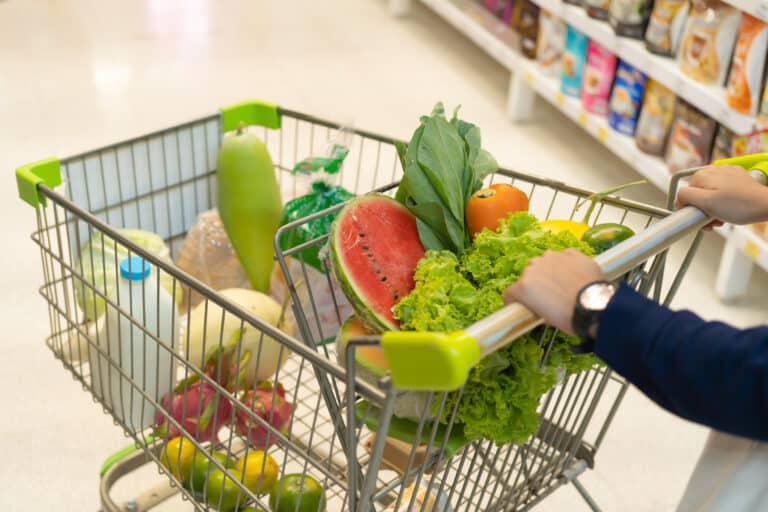 Woman hands buying fruit and vegetable in supermarket on grocery products shelves with shopping cart or trolly. Food in store. People lifestyle